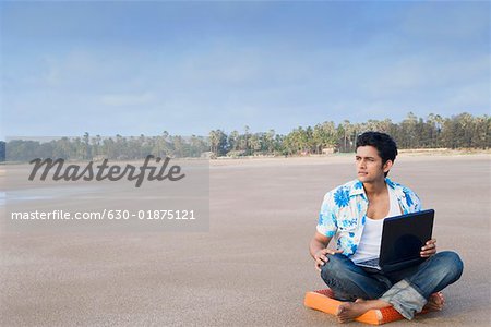 Young man sitting on a cushion and holding a laptop