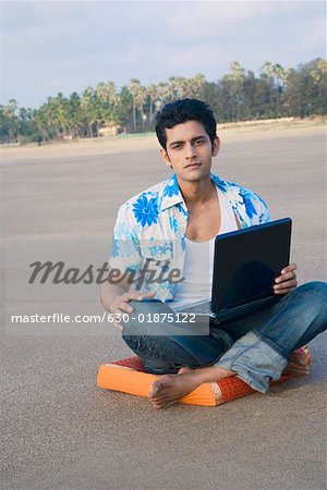 Portrait of a young man sitting on a cushion and holding a laptop