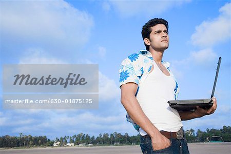 Low angle view of a young man standing on the beach and holding a laptop