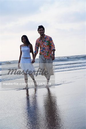 Portrait of a young man holding hands of a young woman and walking on the beach