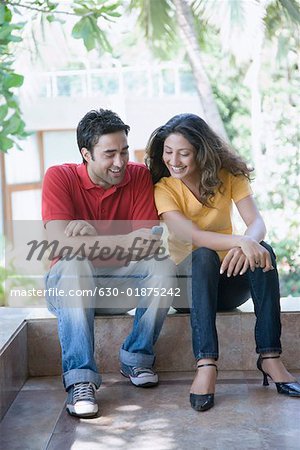 Jeune homme assis avec une jeune femme et SMS sur un téléphone mobile