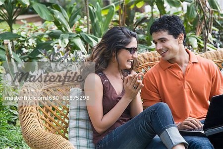 Jeune couple assis avec un ordinateur portable sur un divan et souriant