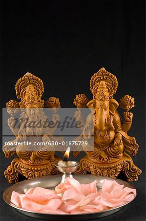 Close-up of an oil lamp and flower petals in front of Hindu gods