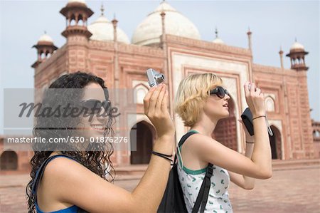 Side profile of two young women taking a picture in front of a mausoleum, Taj Mahal, Agra, Uttar Pradesh, India