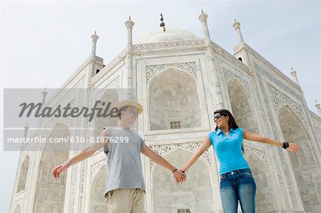 Low angle view of a young couple standing in front of a mausoleum, Taj Mahal, Agra, Uttar Pradesh, India