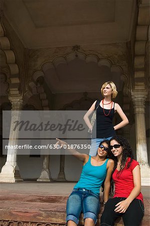 Two young women sitting with their friend standing behind them Taj Mahal, Agra, Uttar Pradesh, India