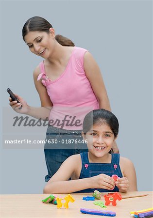 Porträt eines Mädchens, das Lächeln und ihre Mutter hinter ihr Handy halten