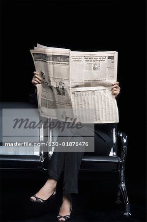 Low section view of a businesswoman sitting on a bench and reading a newspaper