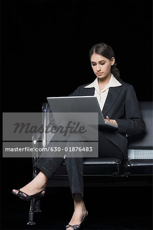 Businesswoman sitting on a bench and using a laptop