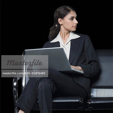 Businesswoman sitting on a bench and using a laptop