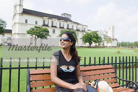 Young woman sitting on a bench with a cathedral in the background, Se Cathedral, Goa, India