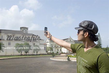 Young man taking a picture of a cathedral with a mobile phone, Se Cathedral, Goa, India