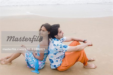 Side profile of a young couple sitting back to back on the beach