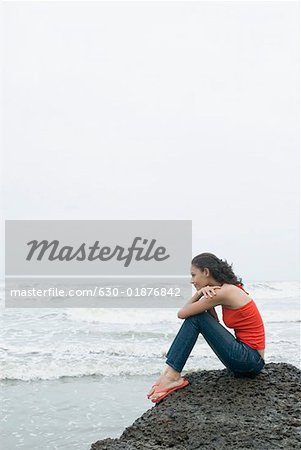 Profil de côté d'une jeune femme assise sur un rocher et en regardant la mer