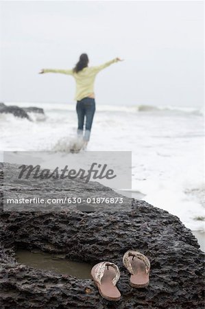 Flip Flops liegt auf einem Felsen mit einer jungen Frau im Hintergrund stehend