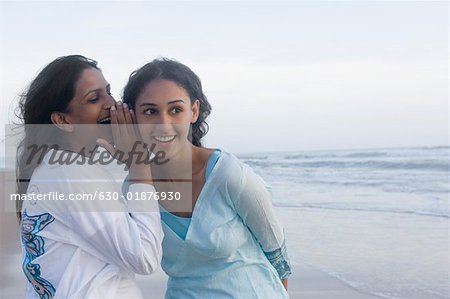 Profil de côté d'une jeune fille chuchoter à l'oreille de son amie sur la plage