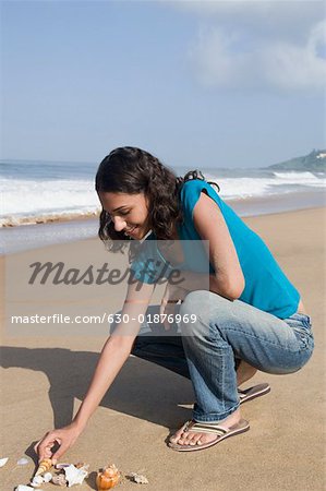 Profil de côté d'une jeune femme jouant avec des coquillages sur la plage