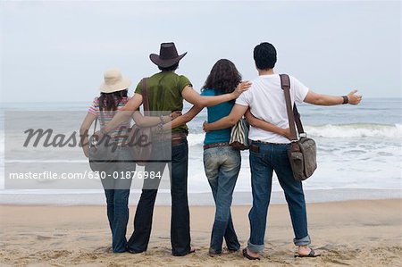 Rear view of two young couples standing on the beach with their arms around each other