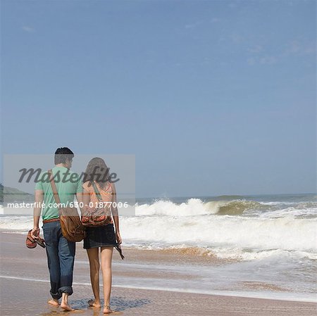 Vue arrière d'un jeune couple tenant leurs pantoufles et marchant sur la plage