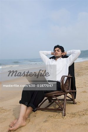 Businessman sitting in an armchair with a laptop on the beach