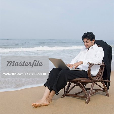 Businessman sitting in an armchair and using a laptop on the beach