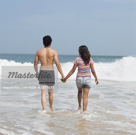 Vue arrière d'un jeune couple, main dans la main et en marchant sur la plage