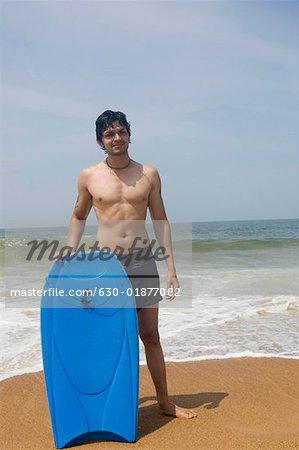 Portrait of a young man standing on the beach and holding a body board