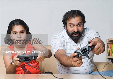 Portrait of a mid adult man sitting on a couch with his daughter and playing video game