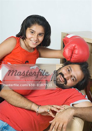 Portrait d'un homme adult moyen, allongée sur un canapé avec sa fille portant des gants de boxe