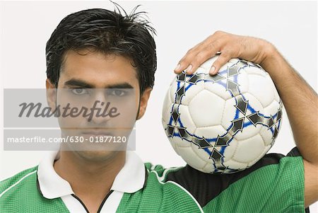 Portrait d'un jeune homme portant un ballon de football sur son épaule