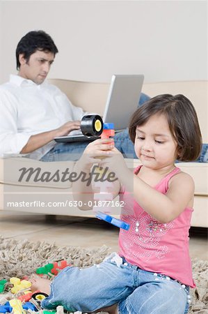 Mädchen spielen mit Spielzeug und ihr Vater arbeitet an einem Laptop im Hintergrund