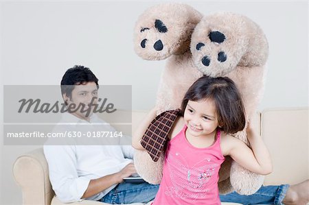 Close-up of a girl holding a teddy bear and her father sitting behind her