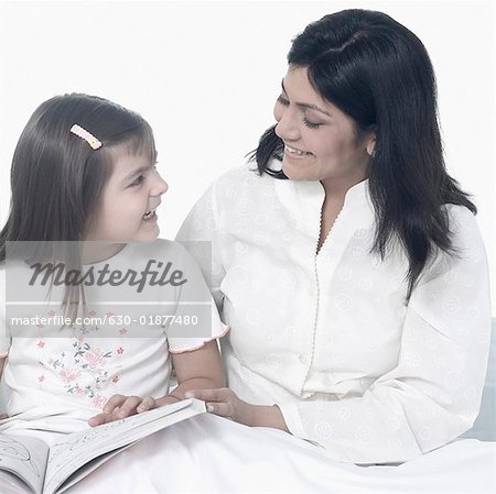 Mid femme adulte avec sa fille assise sur le lit et souriant