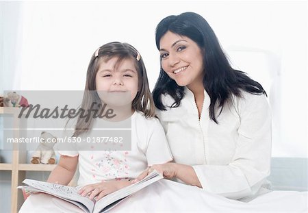Portrait of a mid adult woman sitting with her daughter on the bed and smiling