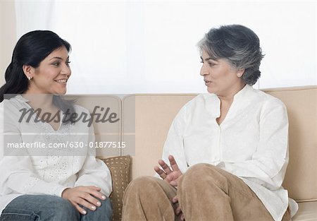 Mature woman and her daughter sitting on a couch and talking to each other