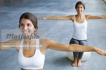 Two teenage girls sitting on fitness balls with arms out, both smiling