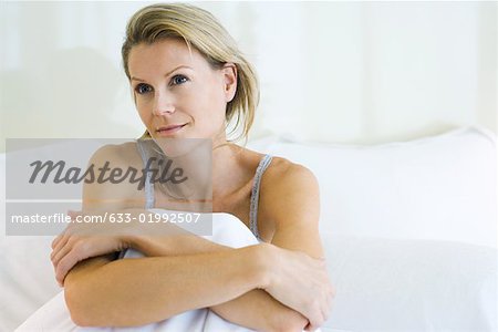 Woman sitting in bed, looking away, smiling