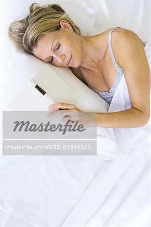Femme endormie dans son lit avec un livre ouvert à côté d'elle