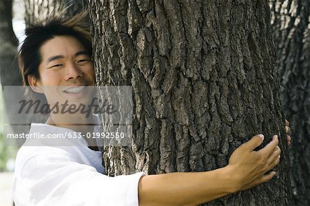 Homme hugging tronc d'arbre, souriant à la caméra