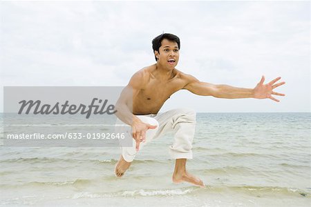 Man jumping in the air and shouting, ocean in background