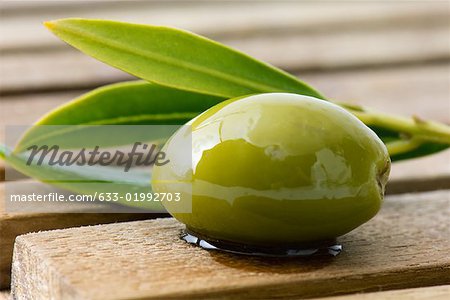 Olive and sprig of leaves on wood table, close-up