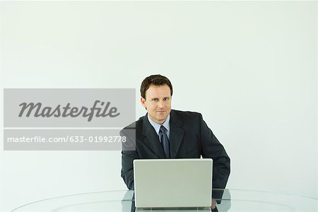 Businessman sitting at desk, using laZSop computer, smiling at camera