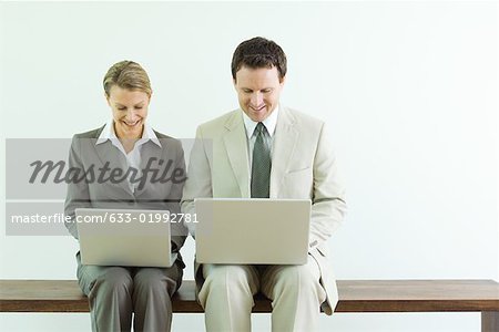 Mâle et femelle entreprise associates assis côte à côte, les deux à l'aide d'ordinateurs laZSop
