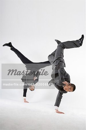 two business men doing handstand with one hand