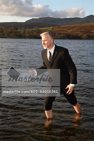 Businessman Walking through Lake with Laptop Computer