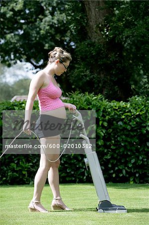 Femme enceinte, tonte de pelouse avec aspirateur nettoyeur