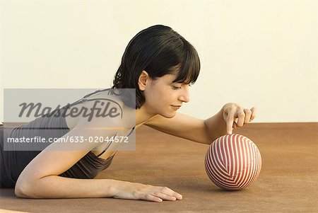 Woman lying on stomach, touching ball with finger, side view
