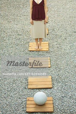 Woman standing opposite sphere on footpath in gravel, high angle view, cropped