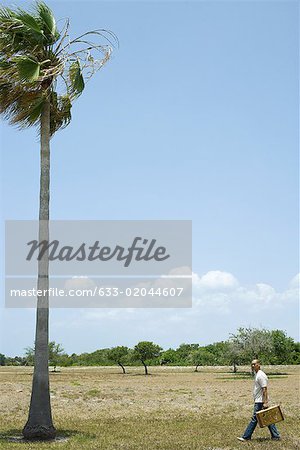 Man walking in tropical landscape, carrying suitcase