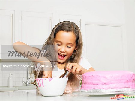 Girl (8-10) dipping finger in icing bowl